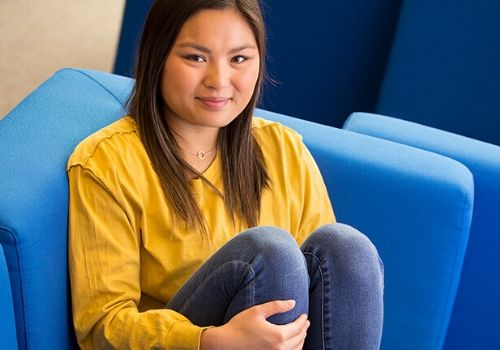 Student in yellow blouse sitting in bright blue chair.